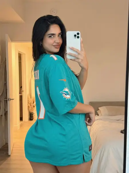 Woman wearing a teal Miami Dolphins jersey taking a mirror selfie in a bedroom