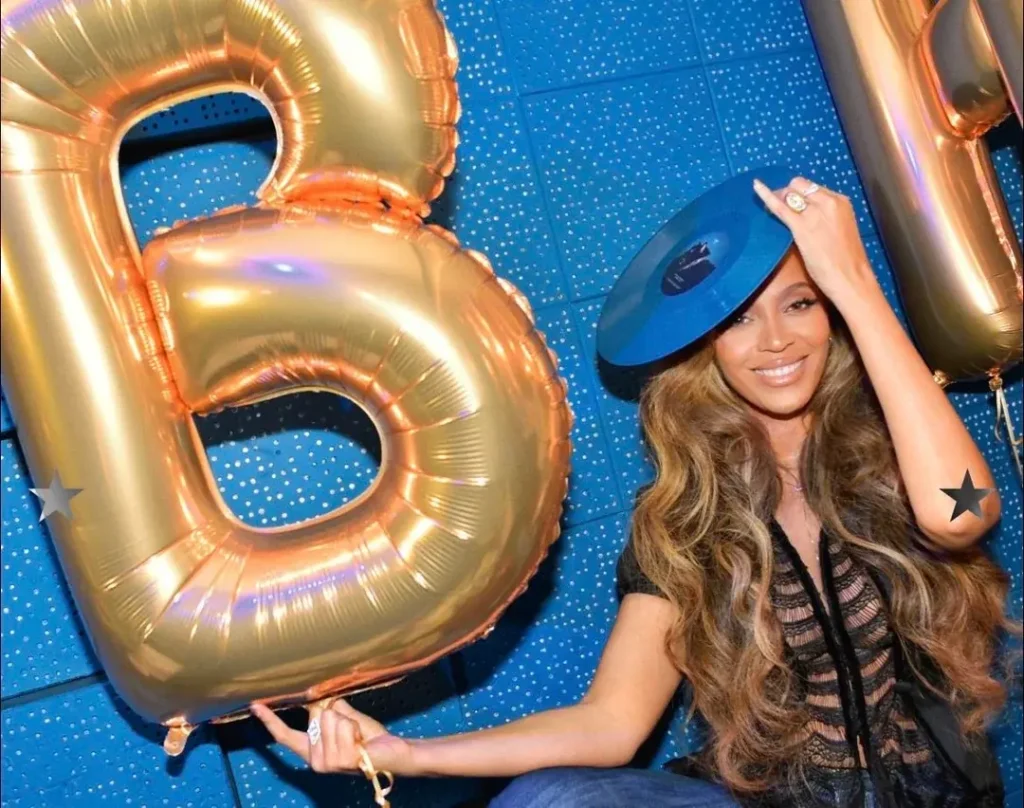Beyoncé wearing blue B'Day vinyl record as hat at anniversary signing event gold B letter balloon 2026